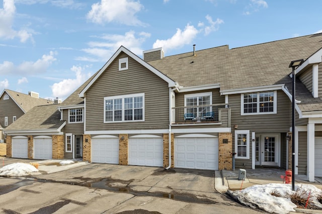 townhome / multi-family property featuring brick siding, french doors, driveway, a balcony, and an attached garage