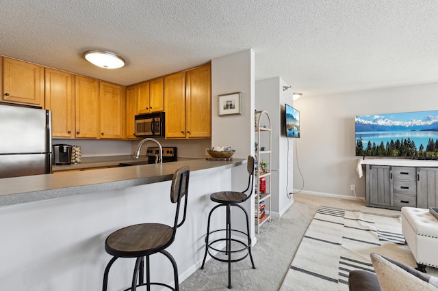 kitchen featuring light carpet, a sink, a kitchen breakfast bar, appliances with stainless steel finishes, and a peninsula