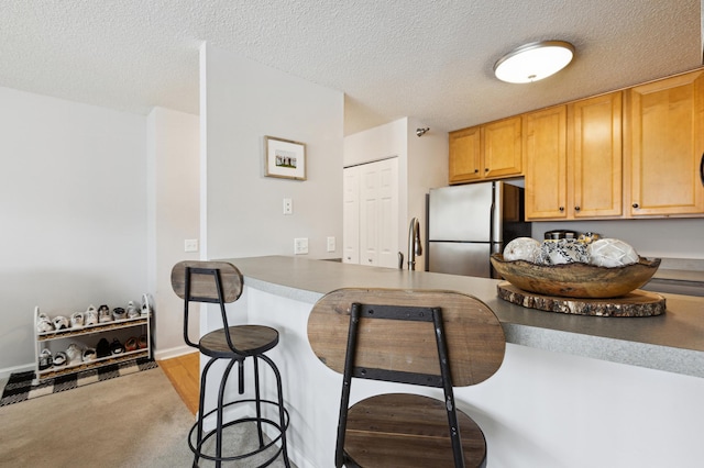 kitchen featuring dark countertops, a breakfast bar area, freestanding refrigerator, and a textured ceiling