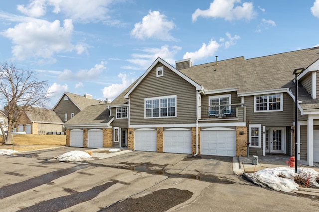 view of front of home with brick siding, driveway, an attached garage, and a balcony