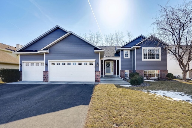 split level home featuring aphalt driveway, an attached garage, brick siding, and a front lawn