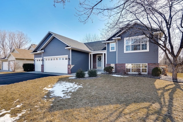 tri-level home with brick siding, an attached garage, a shingled roof, and aphalt driveway