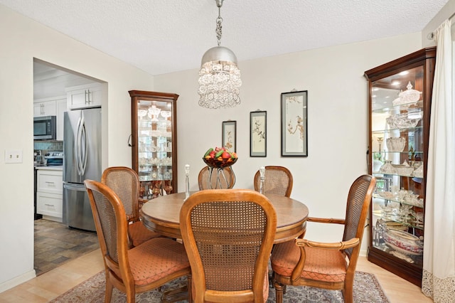 dining room featuring light wood-style floors, a textured ceiling, and a notable chandelier