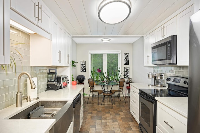 kitchen featuring white cabinets, appliances with stainless steel finishes, stone finish flooring, light countertops, and a sink