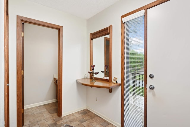 doorway featuring a textured ceiling, stone finish flooring, and baseboards