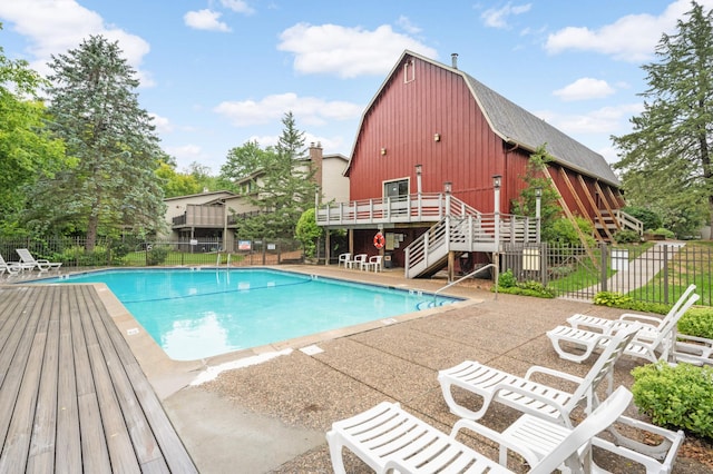 pool featuring stairway, a patio area, fence, a deck, and a barn