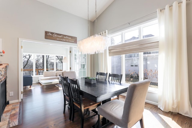 dining area featuring baseboards, a chandelier, a fireplace, wood finished floors, and high vaulted ceiling