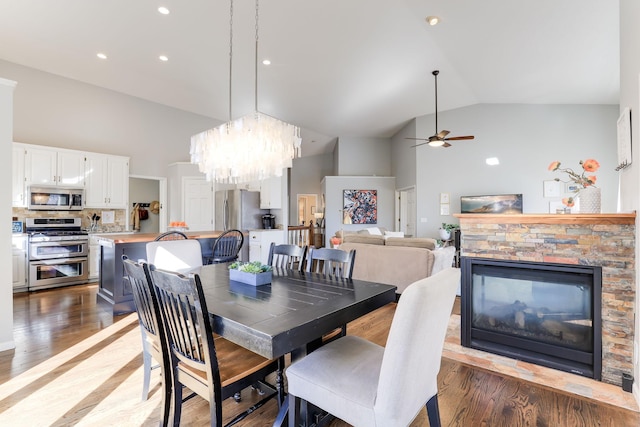 dining area featuring high vaulted ceiling, ceiling fan with notable chandelier, recessed lighting, light wood-style floors, and a stone fireplace