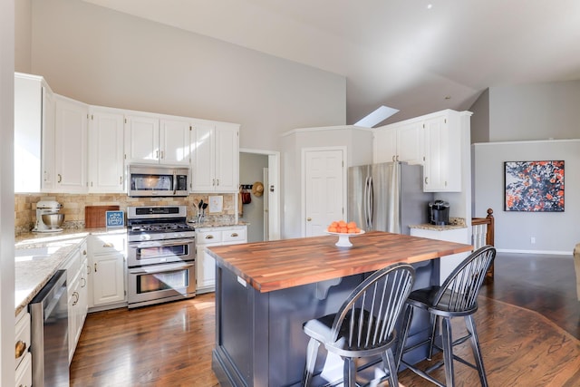 kitchen featuring wooden counters, appliances with stainless steel finishes, white cabinetry, and lofted ceiling