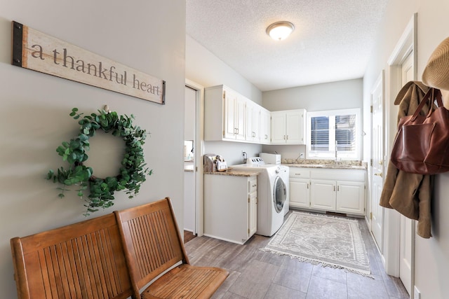 washroom with cabinet space, a sink, light wood-style floors, a textured ceiling, and independent washer and dryer