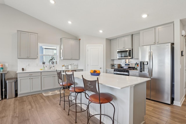 12273 71st Ct NE, Otsego, MN 55330 - kitchen featuring appliances with stainless steel finishes, gray cabinetry, lofted ceiling, a breakfast bar area, and tasteful backsplash