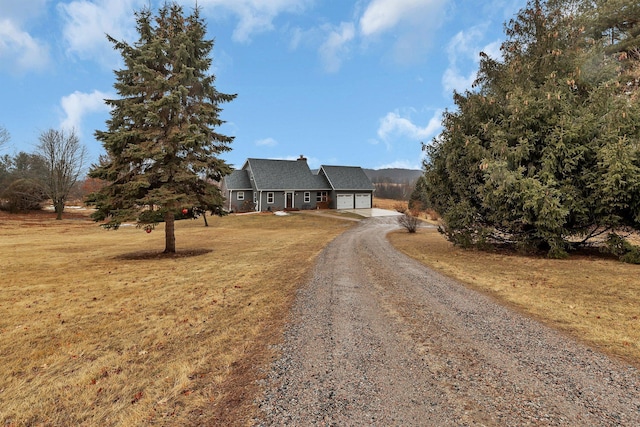 view of front of property featuring an attached garage, driveway, a chimney, and a front yard