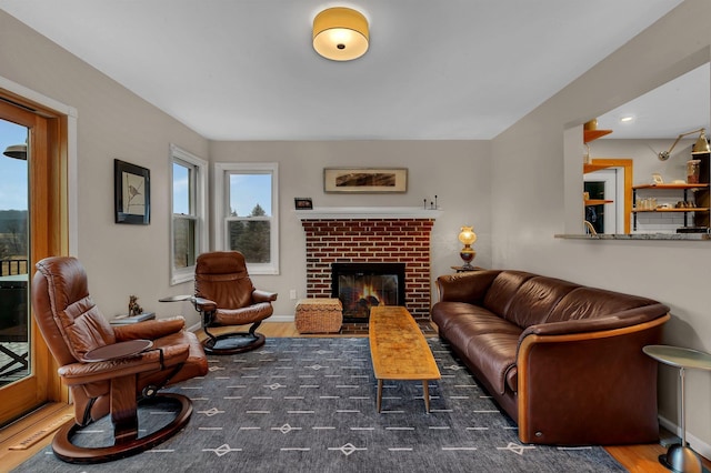 living room featuring a brick fireplace, baseboards, and wood finished floors