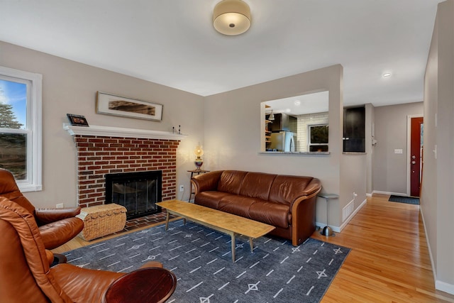 living room featuring a brick fireplace, baseboards, and wood finished floors