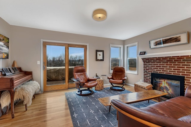 living area featuring baseboards, a brick fireplace, and light wood-style floors