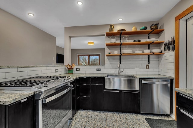 kitchen featuring decorative backsplash, dark cabinets, light stone countertops, stainless steel appliances, and a sink