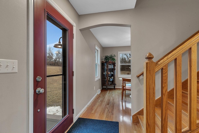 foyer entrance with light wood-style floors, arched walkways, stairway, and baseboards