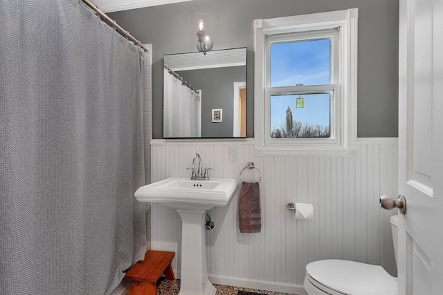 bathroom with a shower with curtain, wainscoting, a sink, and toilet