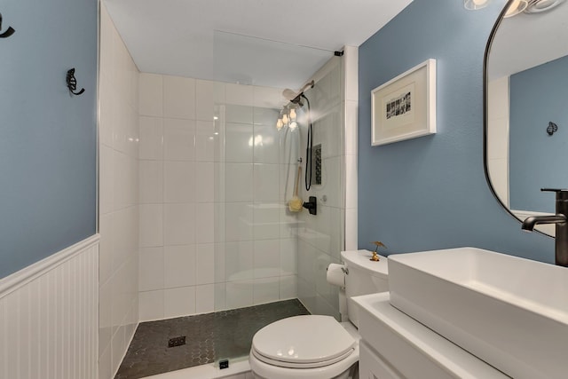 bathroom with a tile shower, wainscoting, a sink, and toilet