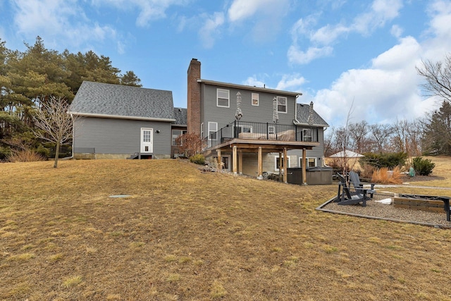 rear view of property featuring a hot tub, a fire pit, a chimney, a deck, and a yard