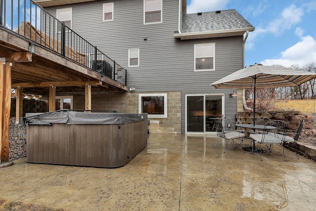 rear view of house featuring stairway, roof with shingles, outdoor dining space, a patio area, and a hot tub