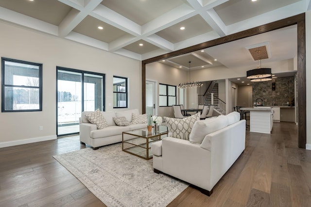 living area featuring baseboards, coffered ceiling, dark wood finished floors, stairs, and beamed ceiling