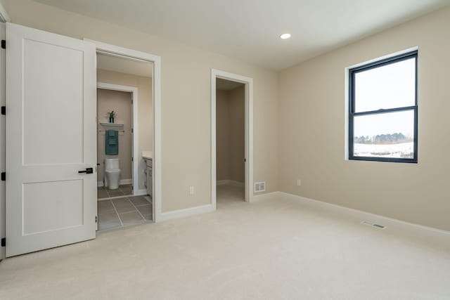 unfurnished bedroom featuring a spacious closet, visible vents, baseboards, light colored carpet, and ensuite bath