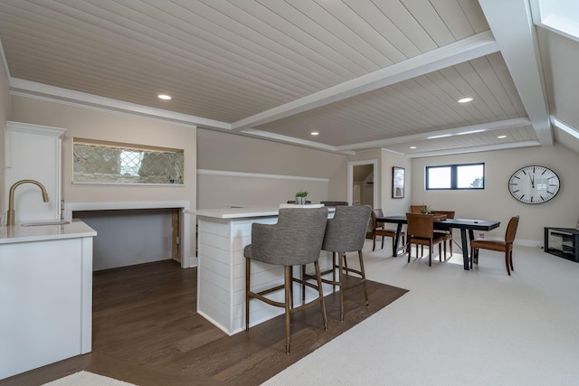 kitchen with beam ceiling, a sink, a kitchen breakfast bar, white cabinetry, and light countertops