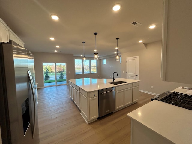 kitchen featuring appliances with stainless steel finishes, an island with sink, a sink, and white cabinets