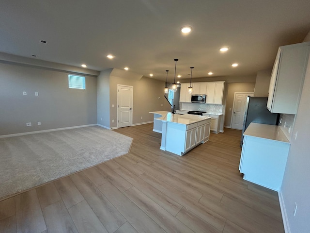 kitchen with a center island with sink, stainless steel appliances, light countertops, light wood-style floors, and a sink