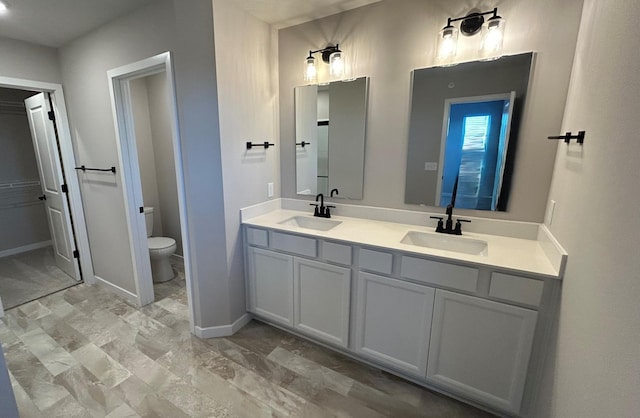 full bathroom with toilet, double vanity, baseboards, and a sink