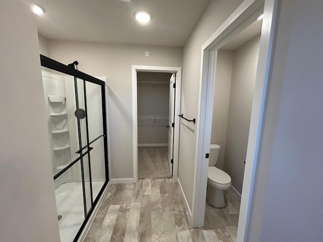 full bathroom featuring baseboards, a shower stall, toilet, and a spacious closet