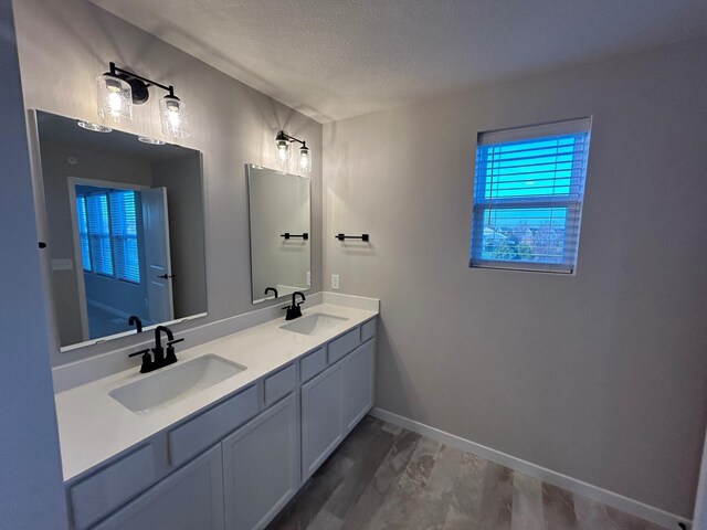 full bathroom with double vanity, a textured ceiling, baseboards, and a sink