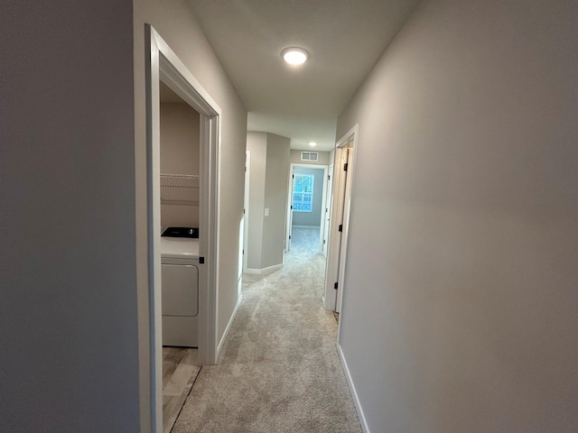 corridor featuring light carpet, washer / clothes dryer, visible vents, and baseboards