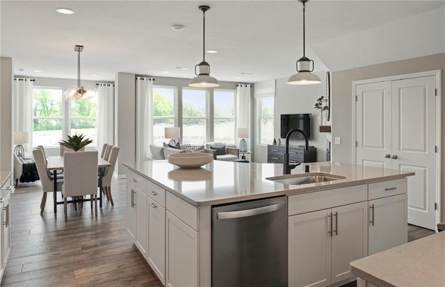 kitchen featuring dark wood-type flooring, a sink, light countertops, dishwasher, and a center island with sink