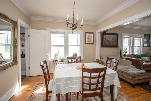 dining space with ornamental molding, a notable chandelier, light wood-style flooring, and baseboards
