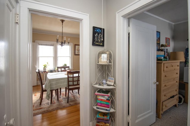 hallway featuring light wood-style flooring, ornamental molding, and a notable chandelier