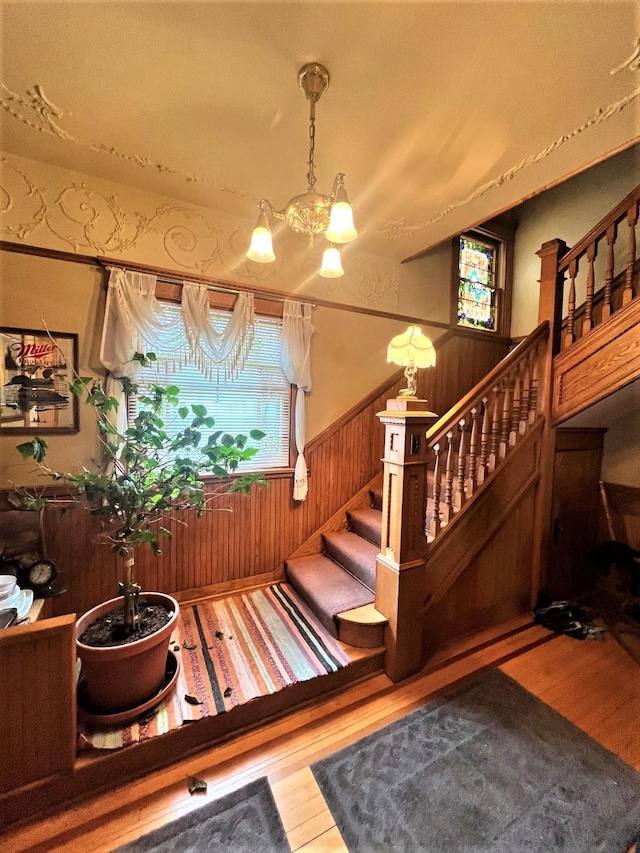 staircase with wainscoting, plenty of natural light, an inviting chandelier, and wood finished floors