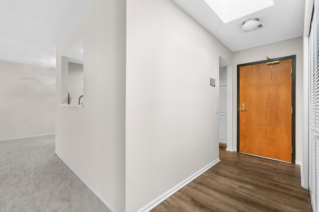 hall featuring a skylight, baseboards, and wood finished floors