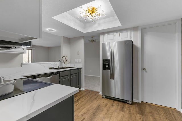 kitchen featuring light wood-style flooring, a sink, stainless steel appliances, a raised ceiling, and a notable chandelier