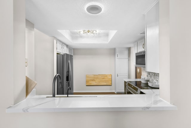 kitchen with a textured ceiling, white cabinetry, stainless steel appliances, decorative backsplash, and a raised ceiling