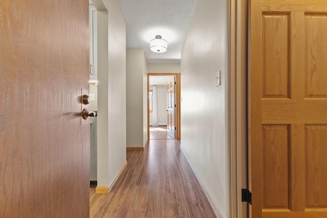 corridor featuring baseboards, a textured ceiling, and wood finished floors