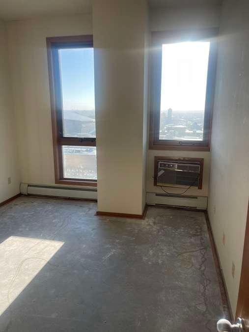 unfurnished room with a healthy amount of sunlight, an AC wall unit, concrete flooring, and a baseboard radiator