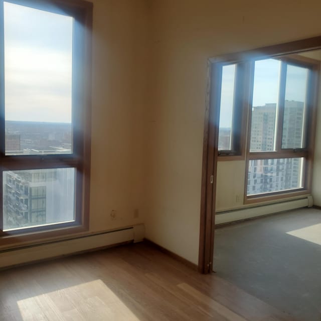 empty room featuring baseboard heating, a healthy amount of sunlight, and wood finished floors