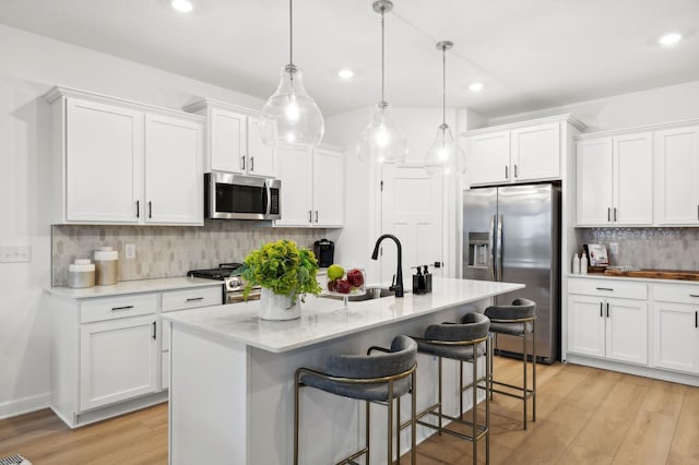 kitchen featuring light wood-style floors, appliances with stainless steel finishes, white cabinets, and a breakfast bar area