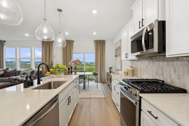 kitchen featuring light countertops, decorative backsplash, appliances with stainless steel finishes, light wood-style floors, and a sink