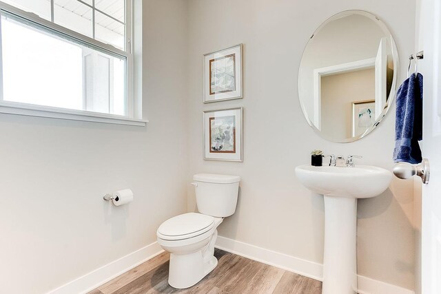 half bath featuring baseboards, toilet, and wood finished floors