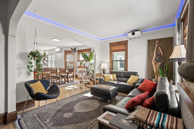 living room featuring arched walkways, a wall mounted AC, baseboards, and wood finished floors