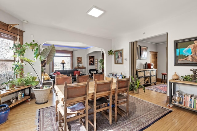 dining area with arched walkways and light wood-style floors