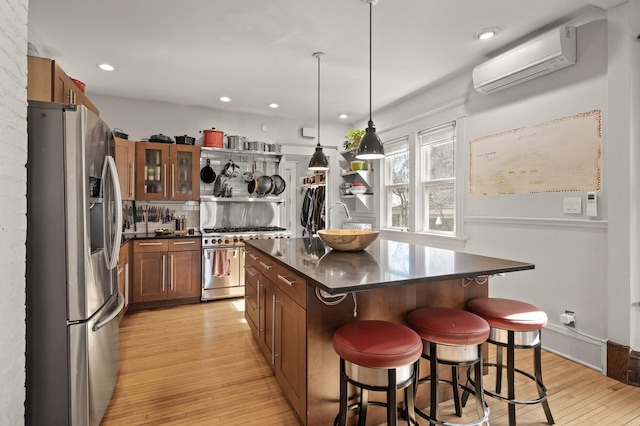 kitchen featuring dark countertops, a wall mounted air conditioner, a kitchen bar, light wood-style flooring, and stainless steel appliances